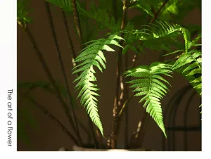 Artificial golden silk fern leaf simulation green plant floral arrangement detail view.