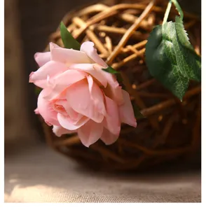 Pink artificial rose flower detail shot with green leaves and woven rattan background.