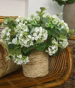 Detailed shot of white artificial snowball flower arrangement in a woven rattan flower pot.