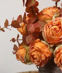Detailed close-up of artificial orange rose bouquet with eucalyptus leaves for home decor.