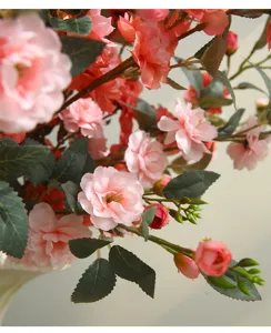 Detailed closeup view of artificial pink camellia flowers with green leaves and stems.
