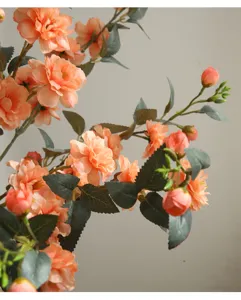 Close-up detail of artificial camellia flower branch with vibrant orange pink petals and green leaves.