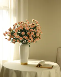 Detail shot of artificial pink rose bouquet in white ceramic vase with open book on table.