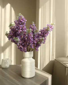 Detailed close-up of artificial lilac flowers in a white ribbed vase for home decor.
