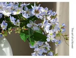 Detaillierte Nahaufnahme künstlicher blauer Blumen mit grünen Blättern in weißer Vase.