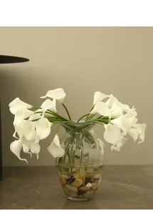 Artificial calla lily flower arrangement in clear glass vase with decorative stones for home.