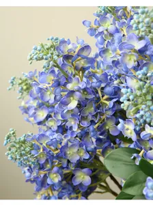 Close-up detail of artificial lilac flower branches, vibrant blue petals and lush green leaves.