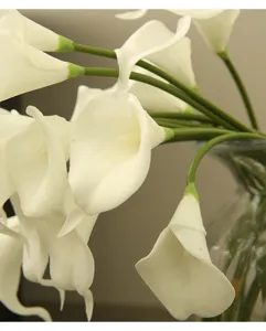 Detailed close-up view of white artificial calla lily flowers with green stems in a glass vase.