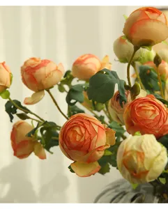 Dettaglio di fiore di rosa artificiale con petali arancioni sfumati e foglie verdi naturali.