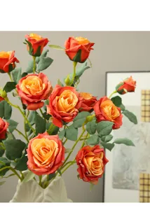 Artificial rose bouquet detail, orange gradient fabric flowers with leaves in white vase.