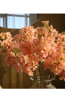 Close-up of pink artificial lilac flowers arrangement in transparent glass vase, indoor decor.