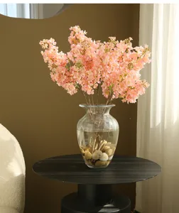 Detailed view of artificial pink lilac flowers bouquet in glass vase with stones for home decor.