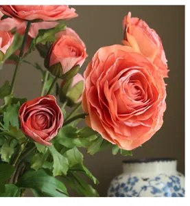 Primo piano dettagliato di fiori artificiali di ranuncolo pesca con foglie, elegante arredo.