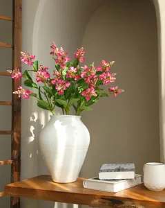 Primer plano detallado de flores artificiales rosas en un florero de cerámica blanca sobre mesa.