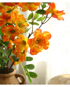 Primo piano dettagliato di fiori di begonia arancioni artificiali, petali vivaci e foglie in vaso.