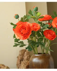 Close-up detail of artificial orange ranunculus bouquet in ceramic vase for interior home decor.