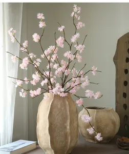 Artificial cherry blossom branch fake flowers in rustic ceramic vase for home decor detail view.