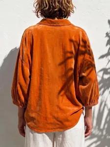 Detail view of the orange velvet long sleeve blouse with lantern sleeves, textured fabric.