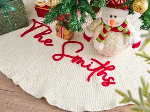Falda de árbol de Navidad tejida y personalizada en marfil con texto bordado en rojo.