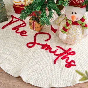 Falda de árbol de Navidad de punto en blanco crema con nombre bordado en rojo.