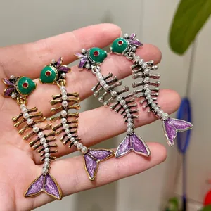 Close-up detail van vintage stijl vis skelet oorbellen met parels en gekleurd emaille.