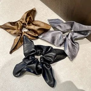 Detalle de coleteros de cuero para el cabello en marrón, gris y negro con pañuelo elegante.