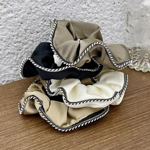 Detailed shot of retro silk hair scrunchies with chic contrast piped edges, soft daily wear.