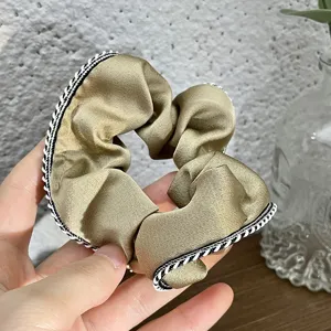 Close-up detail of golden satin hair scrunchie with stylish black white braided edge.