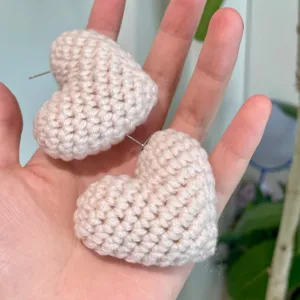 Gros plan de boucles d'oreilles cœur en tricot de laine, design peluche 3D, détail de bijoux.
