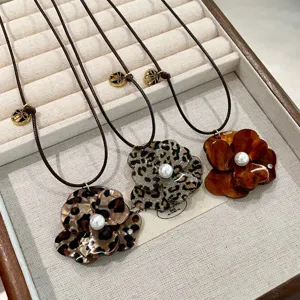 Close-up details of resin flower pendant necklaces with faux pearls and braided cord chains.