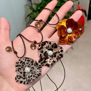 Detail view of flower pendant necklace featuring acrylic leopard print design and central pearl accent.