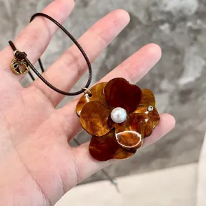 Tortoise shell flower pendant necklace with faux pearl center and brown cord for women.