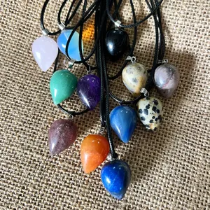 Natural crystal teardrop pendant detail shot, multi-color gemstone necklace on rustic burlap.