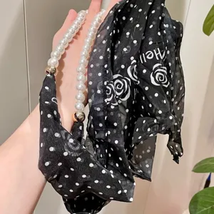 Detail view of a stylish black and white polka dot scarf with pearl chain necklace.