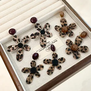 Close-up detail of stylish leopard print flower earrings displayed on a beige velvet tray.