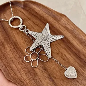 Close-up detail shot of silver Y2K star and flower necklace pendant charm on wooden tray.