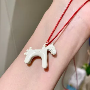 Close-up detail of a charming white enamel 3D pony pendant necklace with a bright red cord.