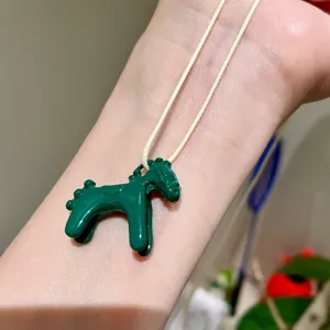 Close up of a cute green enamel horse pendant necklace worn on wrist, exquisite jewelry detail
