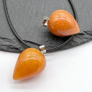 Close-up detail of orange gemstone teardrop pendants with black cord on slate background.