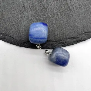 Detailed close-up of blue crystal square stone pendant with silver bail on textured surface.