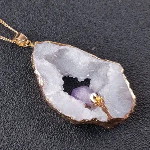 Primo piano del ciondolo in cristallo geode naturale con bordo dorato e pietra viola.