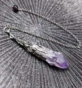 Close-up detail shot of a natural amethyst crystal pendulum necklace with silver cage.
