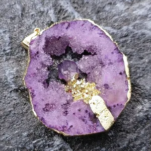 Primo piano ciondolo geode ametista naturale, dettaglio cristallo irregolare dorato.