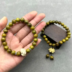 Détail en gros plan du bracelet de perles en bois de santal vert avec pendentif lotus sculpté.