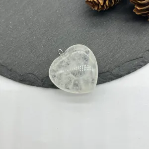 Detailed shot of clear quartz crystal heart pendant with silver bail on slate surface.