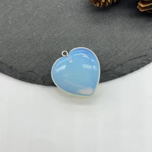 Detail shot of a heart-shaped opalite pendant with a silver bail resting on a dark stone surface.
