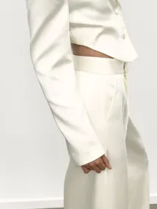 Detailansicht des eleganten weißen kurzen Blazers und der hochgeschnittenen weiten Hosen.
