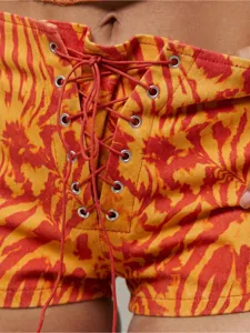 Détail de short taille haute tie-and-dye avec laçage croisé rouge et œillets métalliques.