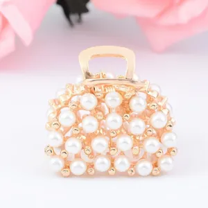 Pince à cheveux dorée en métal ornée de perles nacrées en forme de mini sac à main.