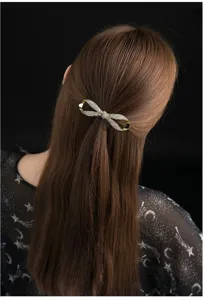 Close-up detail of a gold crystal bow hair clip worn elegantly on dark hair for women.
